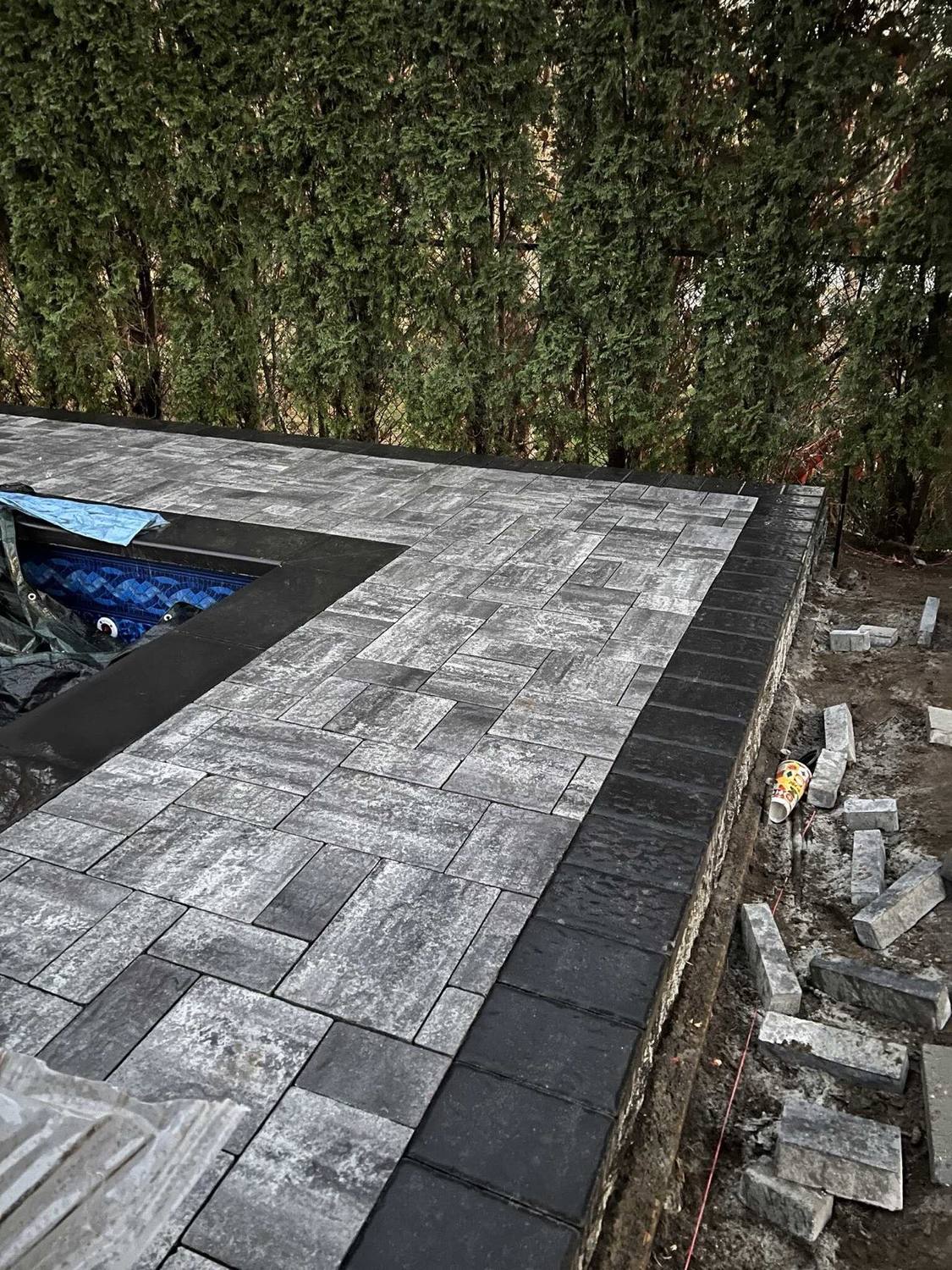 Charcoal coping set over a pool wall beside a plank-pattern paver deck