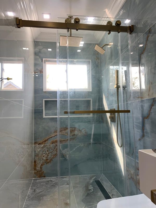 Shower with a brass sliding frame and a window by JDG Concrete & Construction