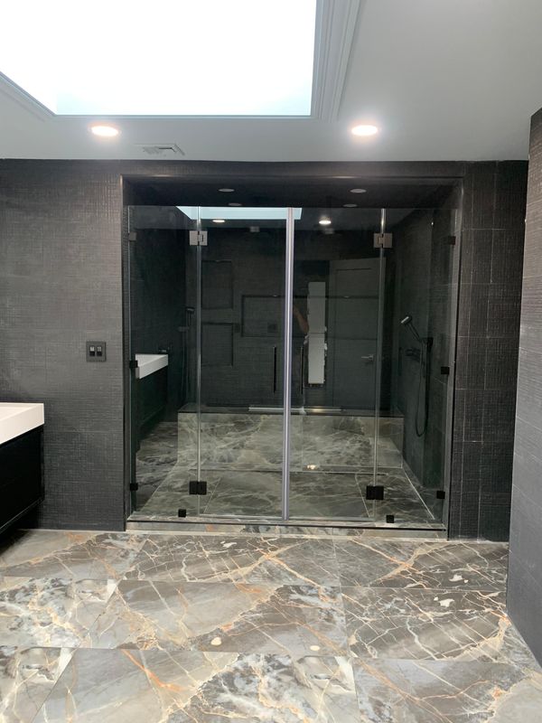 Glass shower enclosure over a marble-look floor by JDG Concrete & Construction
